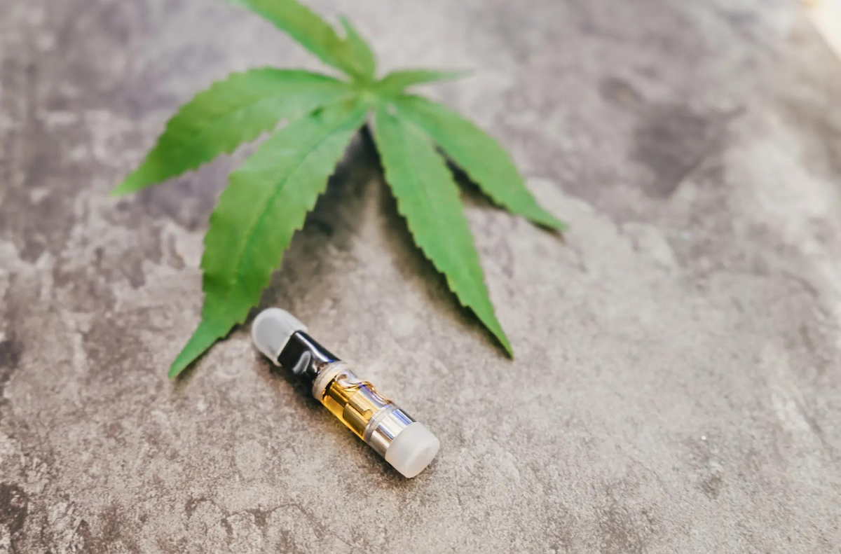 Cannabisový list a vape kazeta na betónovom povrchu