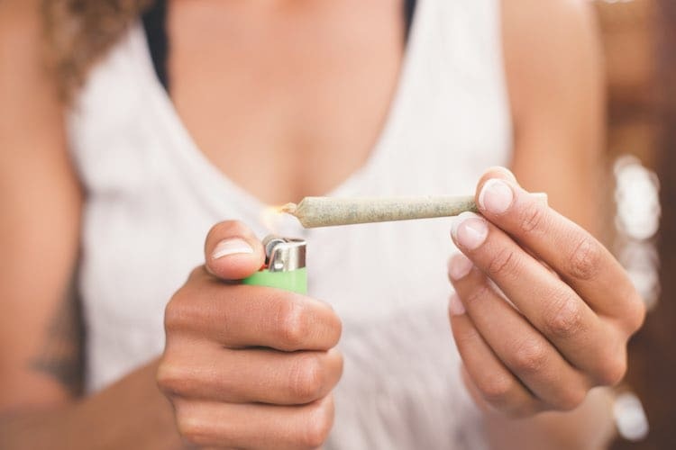 Osoba drží zapálený joint so zeleným zapaľovačom v lifestyle scéne